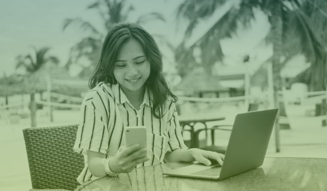 Mulher utilizando celular e computador na praia