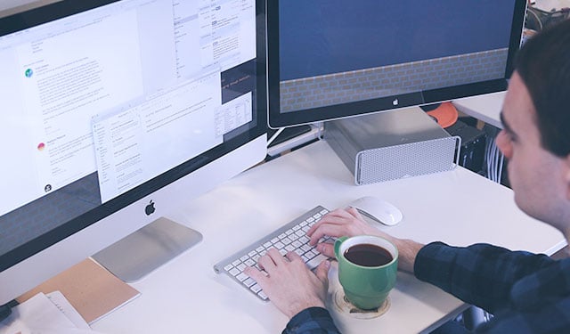 Pessoa utilizando computador em ambiente de trabalho com uma caneca de café