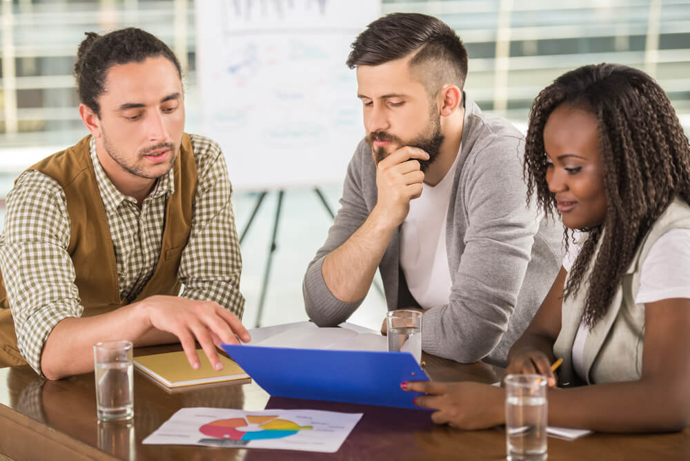 Pessoas em reunião analisando dados em prancheta