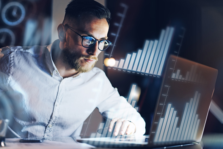 Homem analisando gráficos em um computador e hologramas em primeiro plano