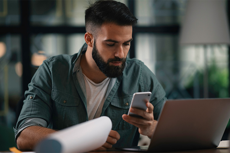 Homem em frente a computador utilizando celular