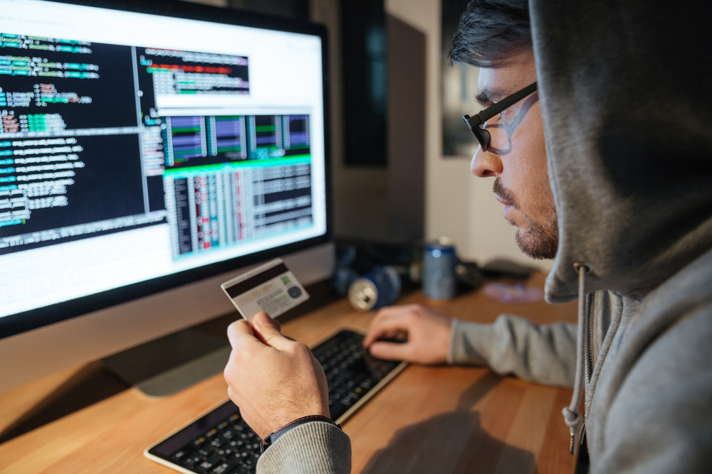 Homem com cartão na mão utilizando computador com tela exibindo códigos