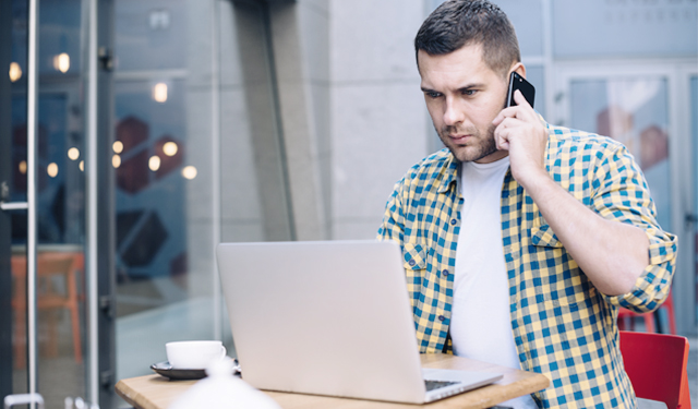 Homem falando ao telefone enquanto utiliza o computador