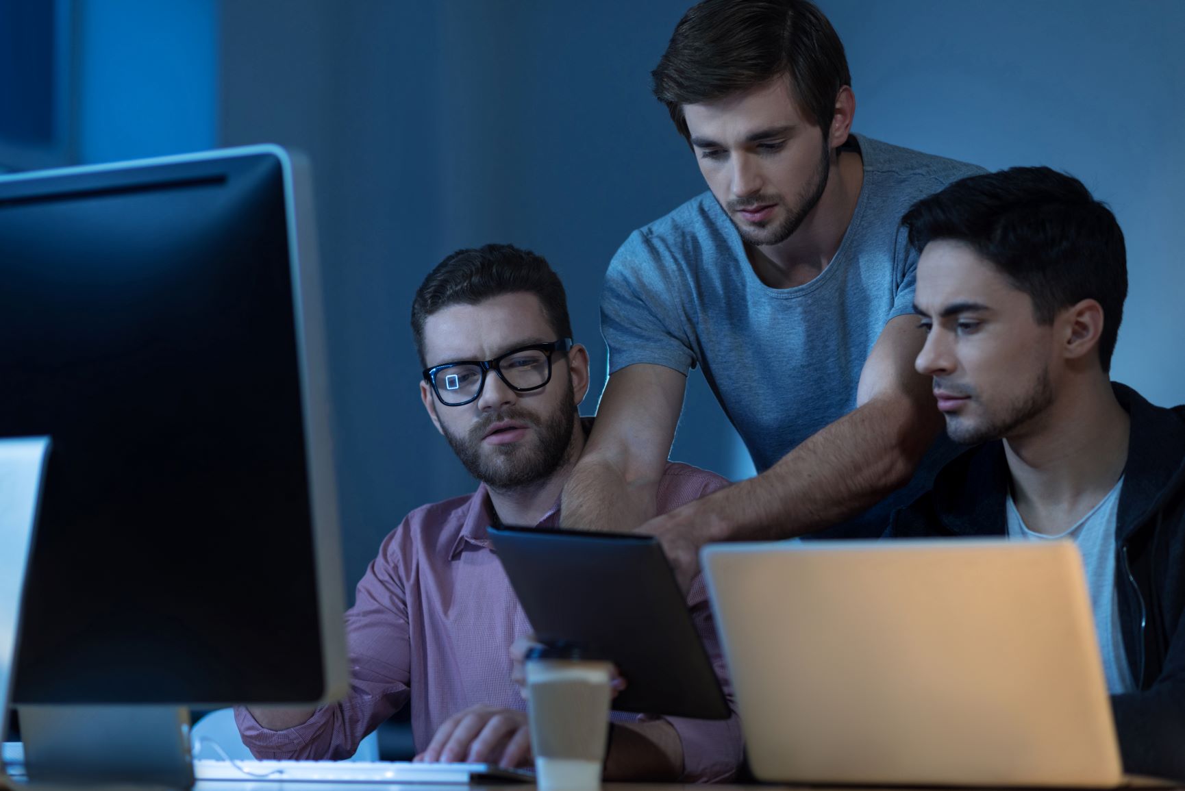 Três homens olhando para telas de computadores e tablet