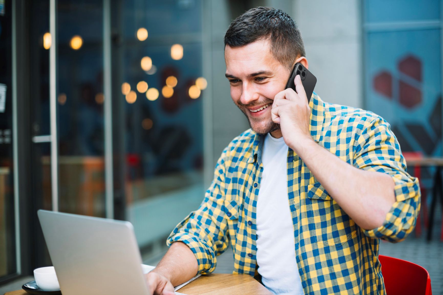 Homem sorrindo falando ao celular e utilizando computador