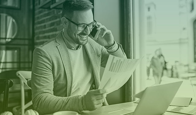 Homem falando ao celular e analisando gráficos financeiros em uma folha de papel