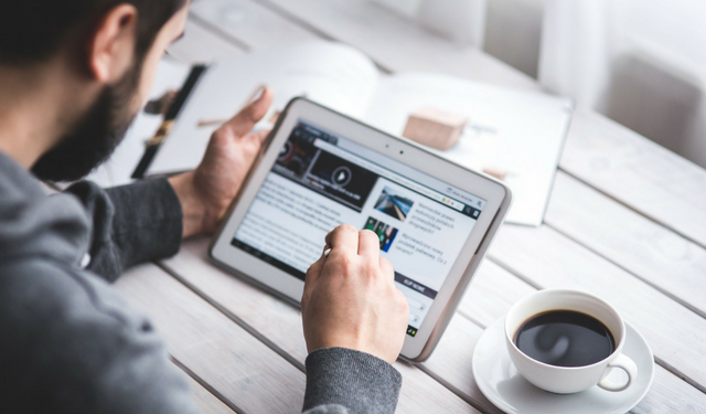 Pessoa tomando um café enquanto lê notícias em um tablet