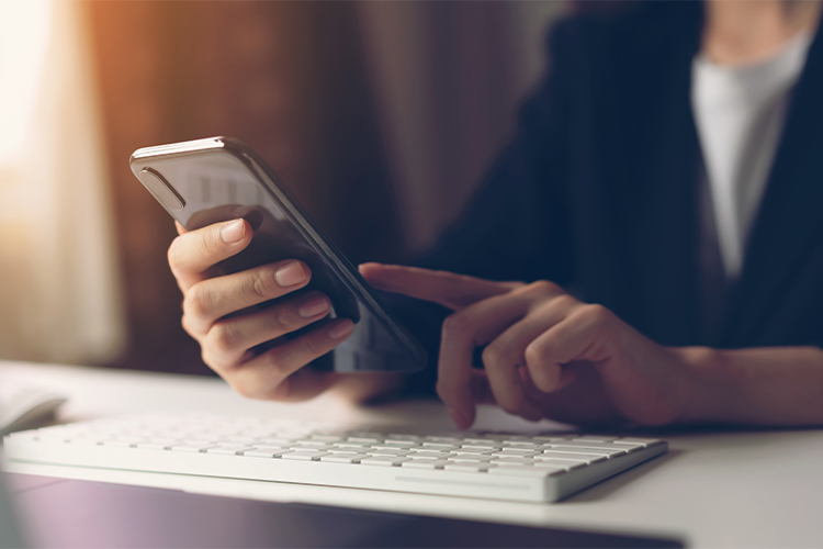 Mulher mexendo no celular que está em cima do teclado