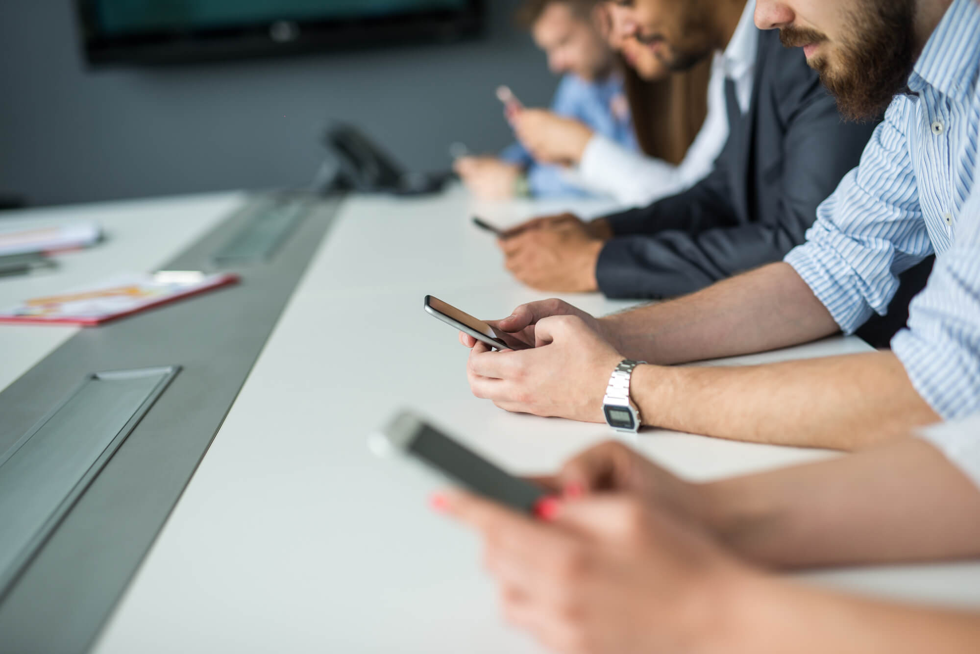 Pessoas em mesa de escritório utilizando celular