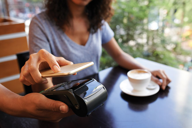 Mulher tomando café utilizando cartão no celular para aproximar da maquininha