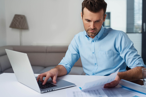 Homem com camisa social utilizando computador e analisando folha