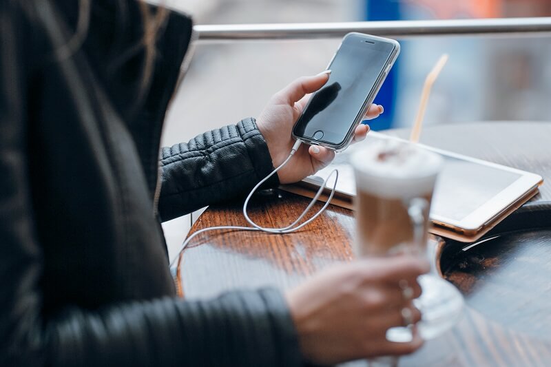 Mulher utilizando celular enquanto toma café