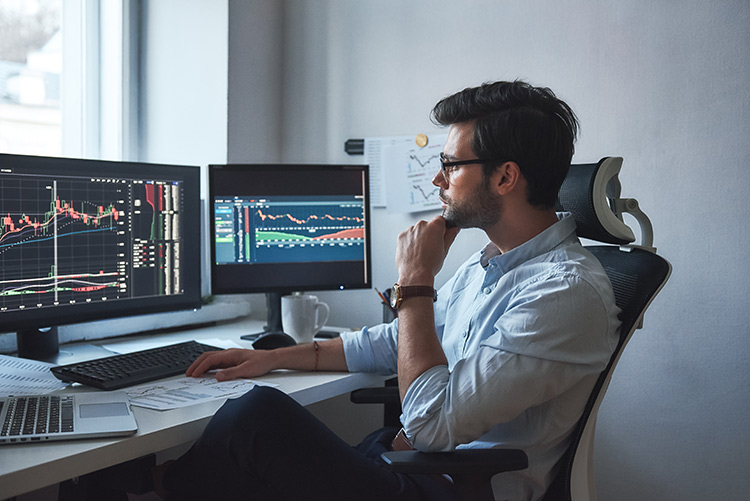 Homem sentado analisando gráficos de ações em computador