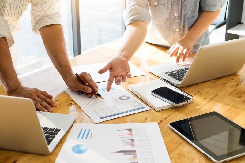 Pessoas em mesa de trabalho analisando folha com gráfico