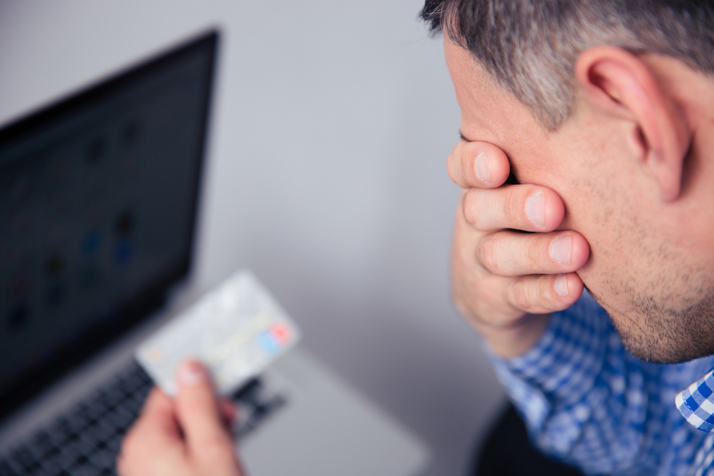 Homem preocupado segurando cartão em frente de um computador